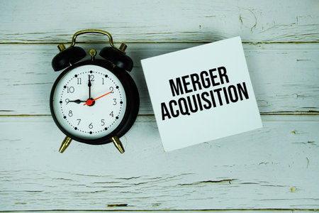 Merger Acquisition text message on sticky note with alarm clock on wooden backgroundの写真素材