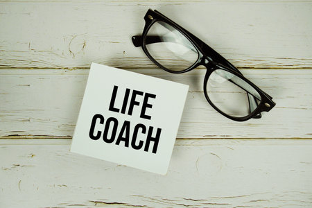 Life Coach text message on sticky note with eyeglasses on wooden backgroundの写真素材