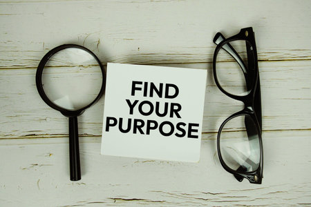 Find Your Purpose text message on sticky note with magnifying glass and eyeglasses on wooden...