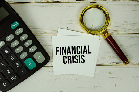Financial Crisis text message on sticky note with magnifying glass and calculator on wooden backgroundの写真素材