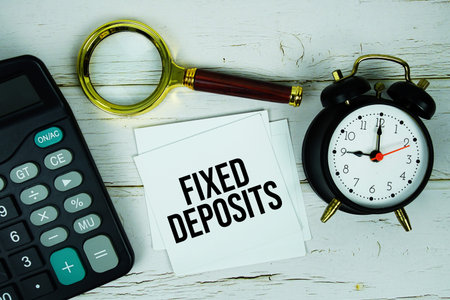 Fixed Deposits text message on sticky note with magnifying glass, alarm clock and calculator on...