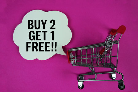 Buy 2 Get 1 Free!! text with speech bubble and trolley shopping cart on pink backgroundの写真素材