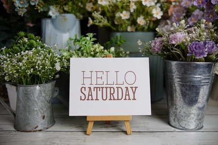Hello Saturday text on paper card with flowers decoration on wooden backgroundの写真素材