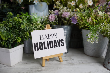 Happy Holidays text on paper card with flowers decoration on wooden backgroundの写真素材