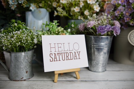 Hello Saturday text on paper card with flowers decoration on wooden backgroundの写真素材