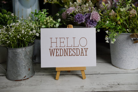 Hello Wednesday text on paper card with flowers decoration on wooden background
