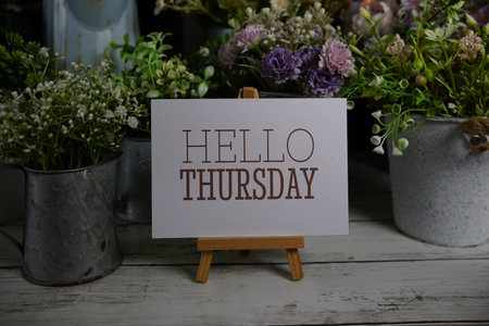 Hello Thursday text on paper card with flowers decoration on wooden background