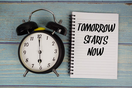 Tomorrow Starts Now text written on notepad with alarm clock on wooden background