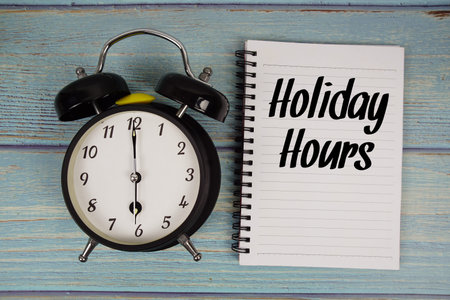 Holiday Hours text written on notepad with alarm clock on wooden background