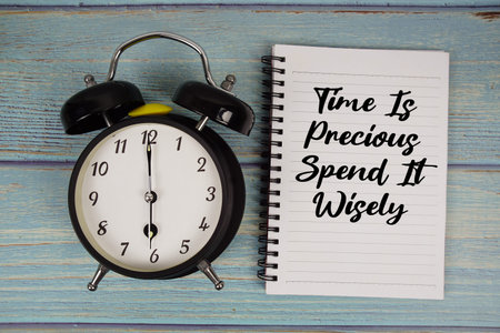 Time is Precious Spend It Wisely text written on notepad with alarm clock on wooden background