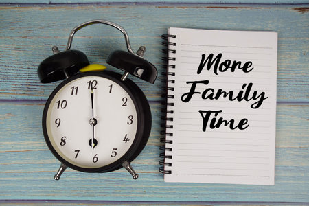 More Family Time text written on notepad with alarm clock on wooden background