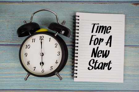 Time For A New Start text written on notepad with alarm clock on wooden background