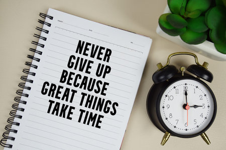 Never give up because great things take time text written on notepad with alarm clock