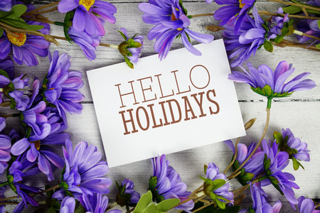 Hello Holidays text with purple flower decoration on wooden background