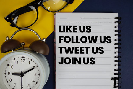 Like Us Follow Us Tweet Us Join Us text written on notepad with alarm clock on blue background
