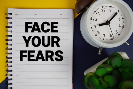 Face Your Fears text written on notepad with alarm clock on blue background