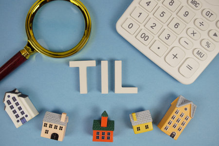 TIL abbreviation of Truth in Lending alphabet letters with house model, magnifying glass and calculator on blue backgroundの写真素材