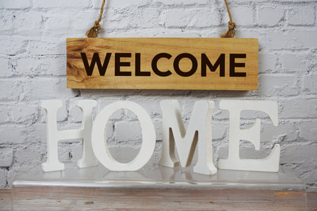 Welcome Home alphabet letters and wooden signboard hanging on white brick wall backgroundの写真素材