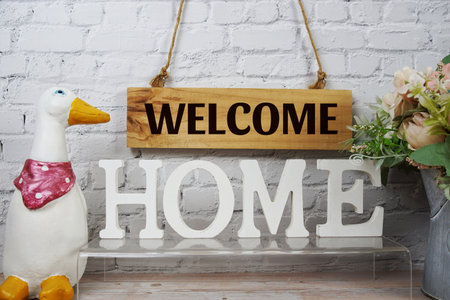 Welcome Home alphabet letters and wooden signboard hanging on white brick wall backgroundの写真素材