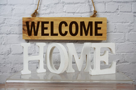 Welcome Home alphabet letters and wooden signboard hanging on white brick wall background