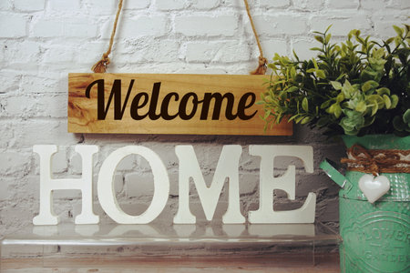 Welcome Home alphabet letters and wooden signboard hanging on white brick wall backgroundの写真素材