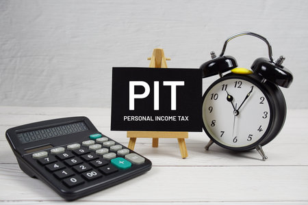 PIT abbreviation of Personal Income Tax text with alarm clock on wooden backgroundの写真素材