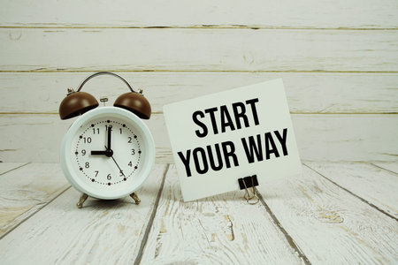 Start Your Way text on paper card with alarm clock on wooden background