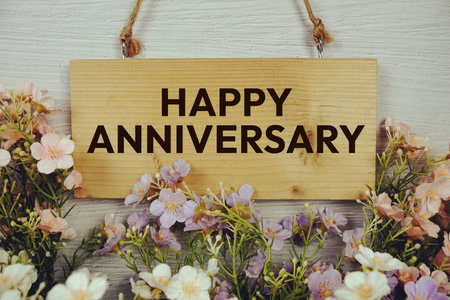 Happy Anniversary text on wooden signboard hanging with flowers decoration on concrete backgroundの写真素材