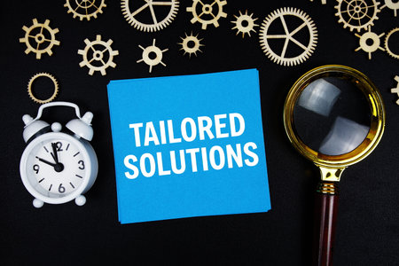 Tailored Solutions text message on sticky note with magnifying glass and alarm clock on black backgroundの写真素材