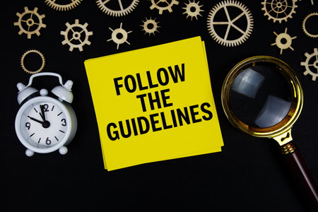 Follow the Guidelines text message on sticky note with magnifying glass and alarm clock on black backgroundの写真素材