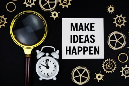 Make Ideas Happen text message on sticky note with magnifying glass and alarm clock on black backgroundの写真素材