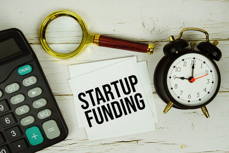 Startup Funding text message on paper with magnifying glass, calculator and alarm clock on wooden backgroundの写真素材