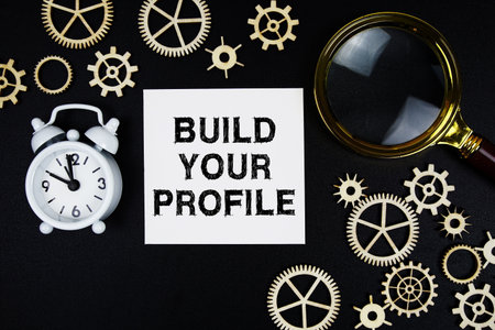 Build Your Profile text message on sticky note with magnifying glass and alarm clock on black backgroundの写真素材