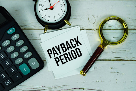 Payback Period text message on paper with magnifying glass, calculator and alarm clock on wooden backgroundの写真素材