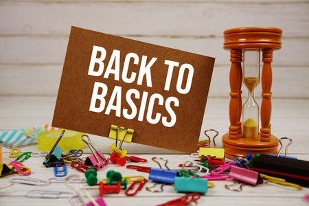 Back To Basics text on paper card with hourglass and stationary on wooden background