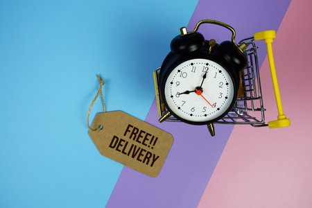 Free Delivery text on price tag with alarm clock and trolley shopping cart on pink, purple, blue geometric backgroundの写真素材