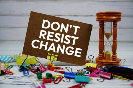 Don't Resist Change text on paper card with hourglass and stationary on wooden background