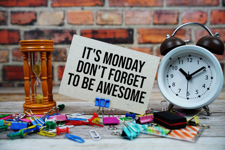 It's Monday Don't Forget To Be Awesome text on paper card with alarm clock and stationary on wooden...