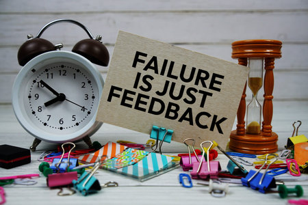 Failure Is Just Feedback text on paper card with alarm clock and stationary on wooden background