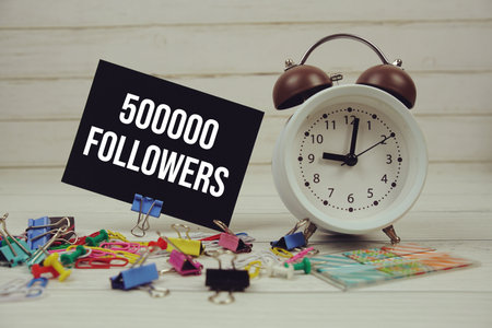 500000 Followers text on paper card with alarm clock and stationary on wooden backgroundの写真素材