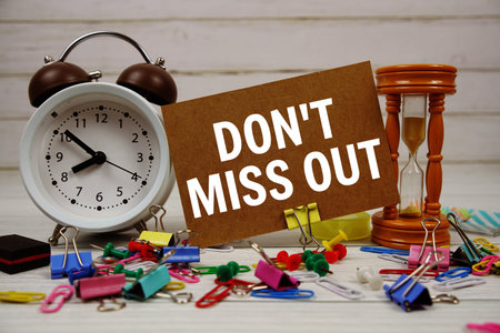 Don't miss out text on paper card with alarm clock and stationary on wooden background