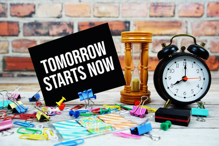 Tomorrow Starts Now text on paper card with hourglass and stationary on wooden background