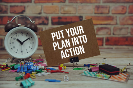 Put Your Plan Into Action text on paper card with alarm clock and stationary on wooden backgroundの写真素材