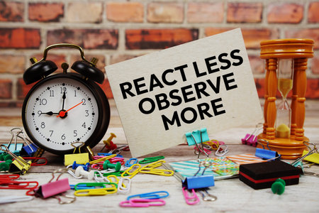 React Less Observe More text on paper card with alarm clock and stationary on wooden background