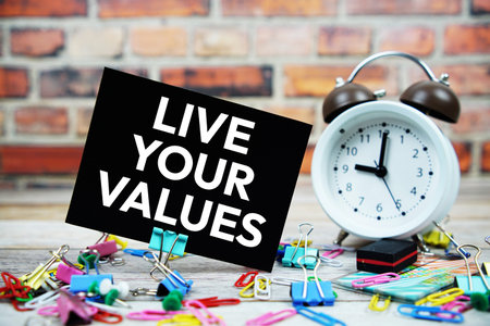 Live Your Values text on paper card with alarm clock and stationary on wooden background