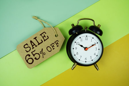 Sale 65% off text on price tag with alarm clock on green, yellow geometric background