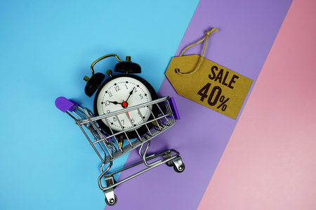 Sale 40% text on price tag with alarm clock and trolley shopping cart on pink, purple, blue...