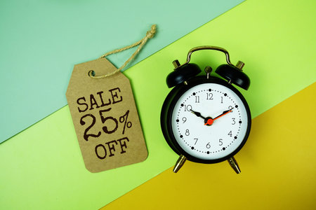 Sale 25% off text on price tag with alarm clock on green, yellow geometric background