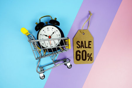 Sale 60% text on price tag with alarm clock and trolley shopping cart on pink, purple, blue geometric backgroundの写真素材