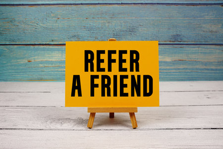 Refer a Friend text written on paper card on wooden backgroundの写真素材